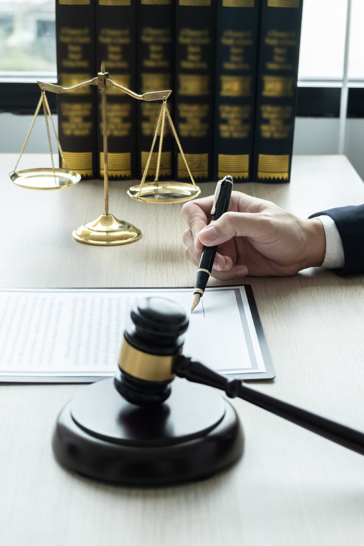 Gavel, brass scales of justice and law books beside a suited hand signing a document