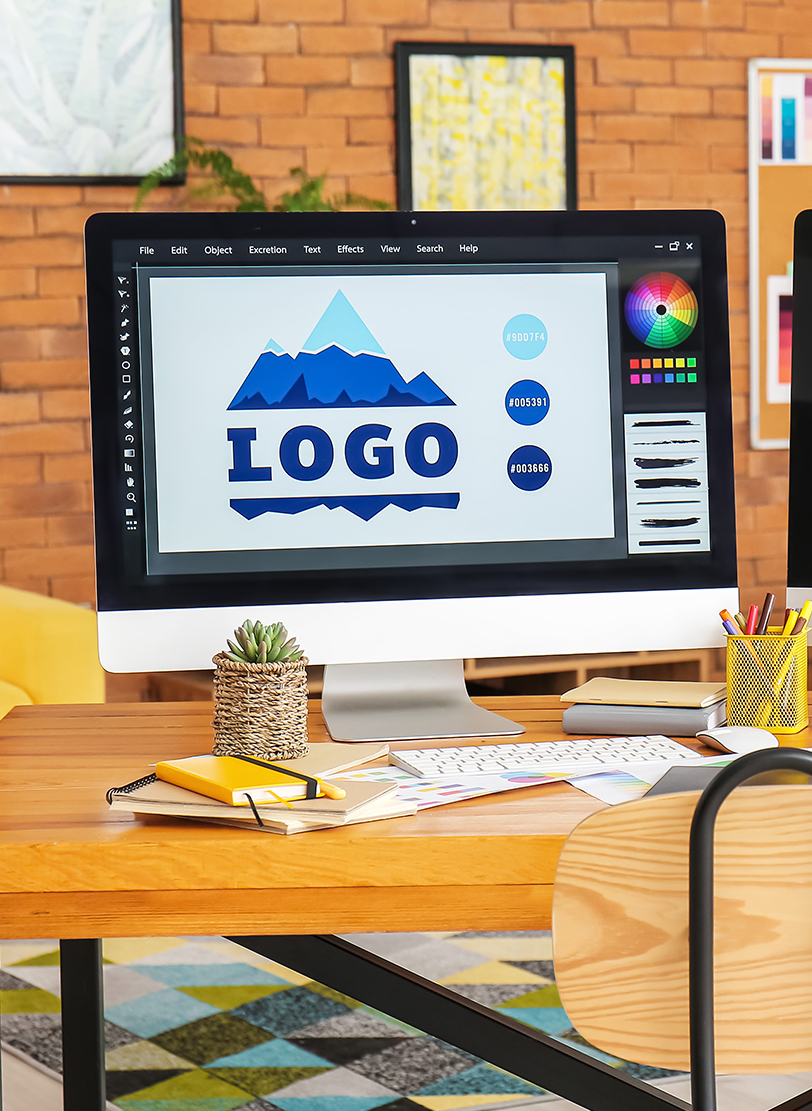 Design software on a monitor showing a blue mountain logo beside its hex colour swatches