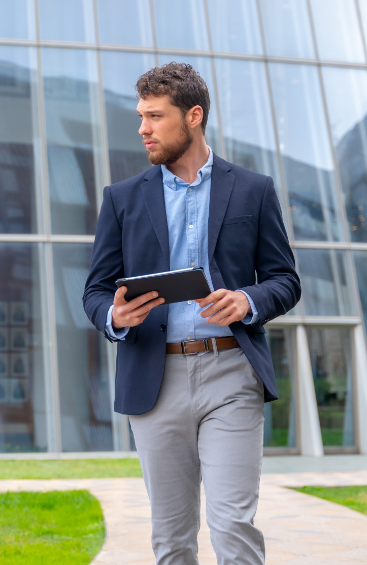 Man in a navy blazer holding a tablet outside a glass office building