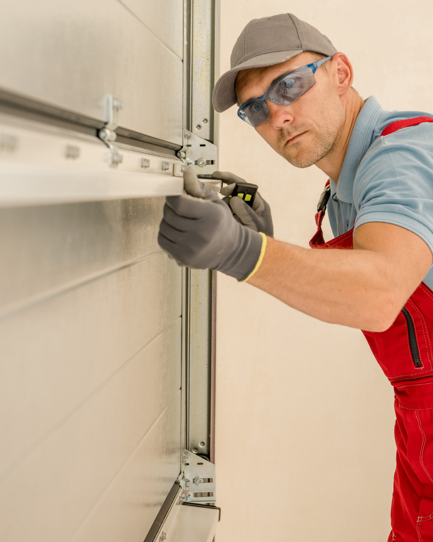 Technician in red overalls and safety glasses adjusting the track hardware on a garage door