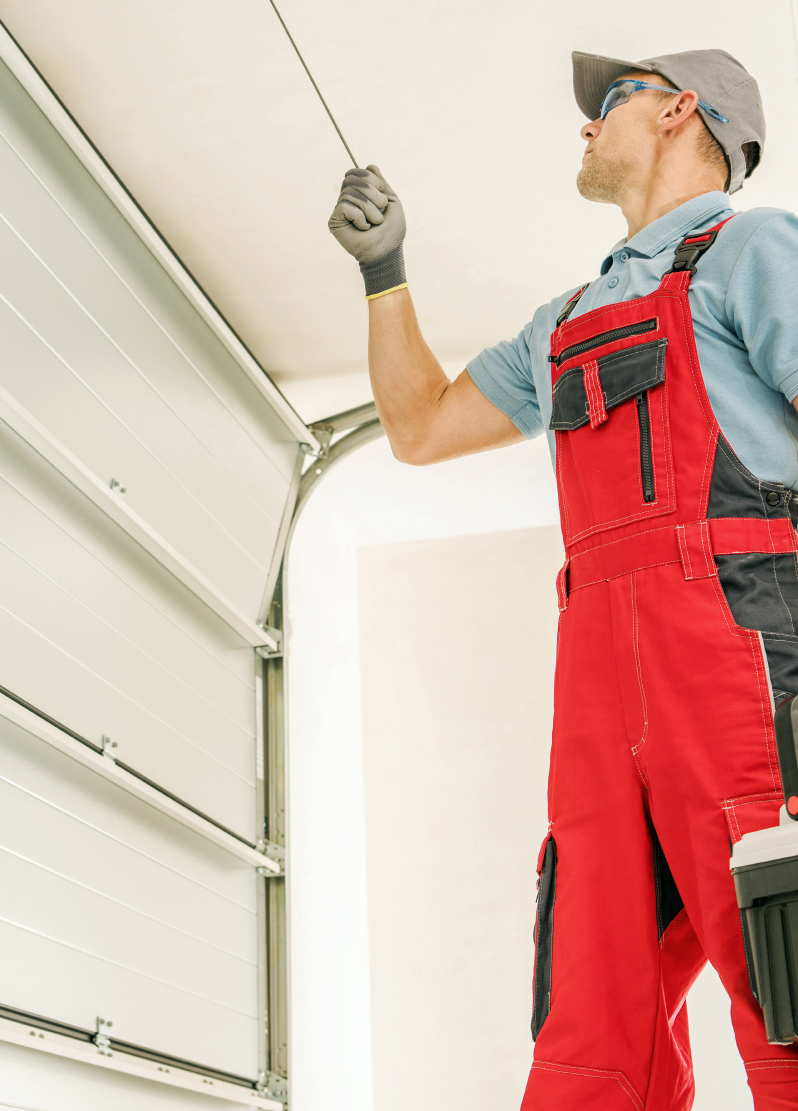 Worker in red overalls pulling the emergency release cord on a white sectional garage door