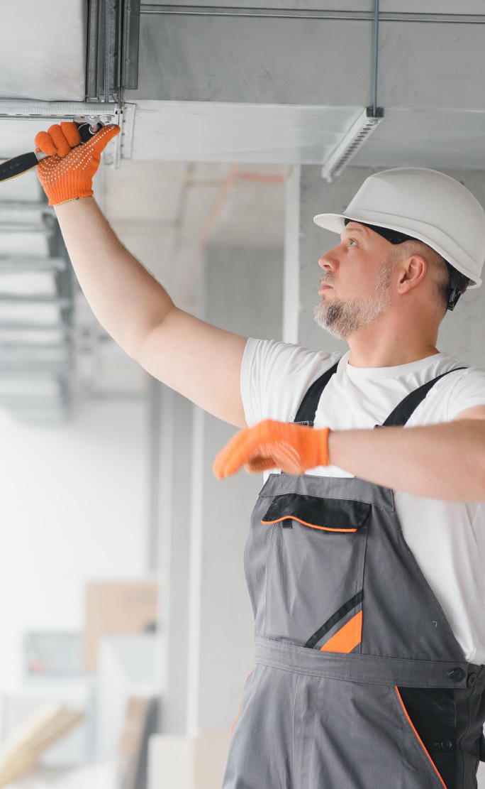 Worker in a hard hat and orange gloves fitting a tool to overhead ductwork
