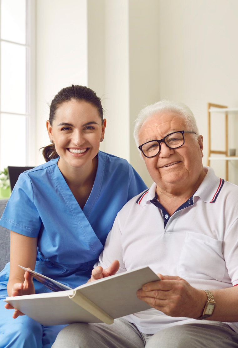Caregiver in blue scrubs and an older man with glasses looking through an open binder together
